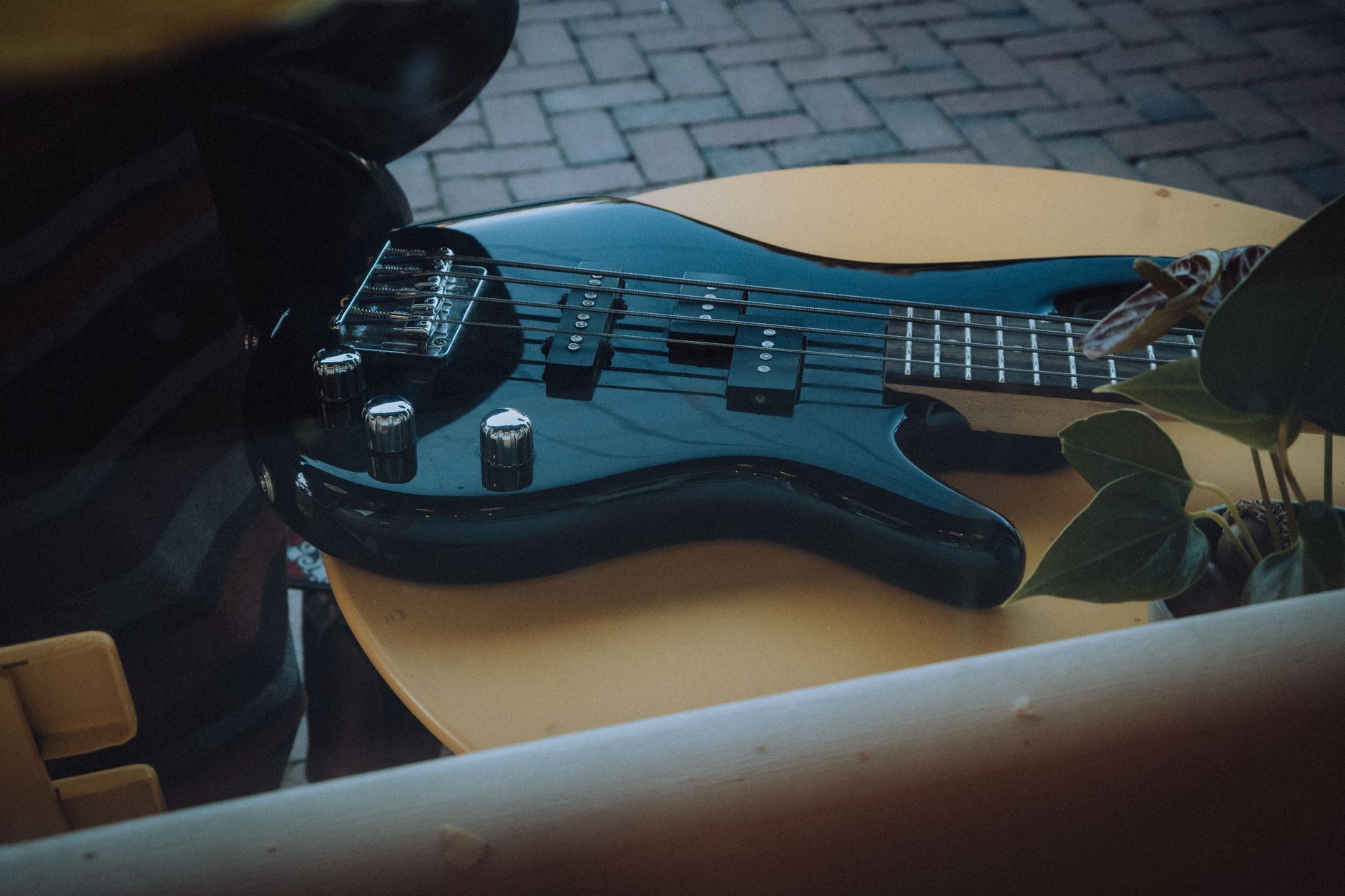 Close-up of an electric bass guitar placed on a table, showcasing its sleek design in an outdoor caf&eacute; setting.