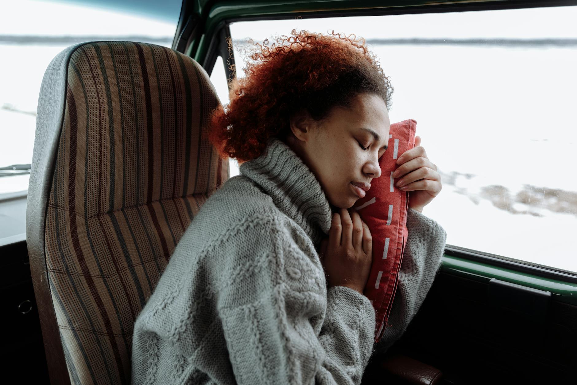 A peaceful moment of a woman sleeping in a campervan, wrapped in a cozy sweater during a winter road trip.