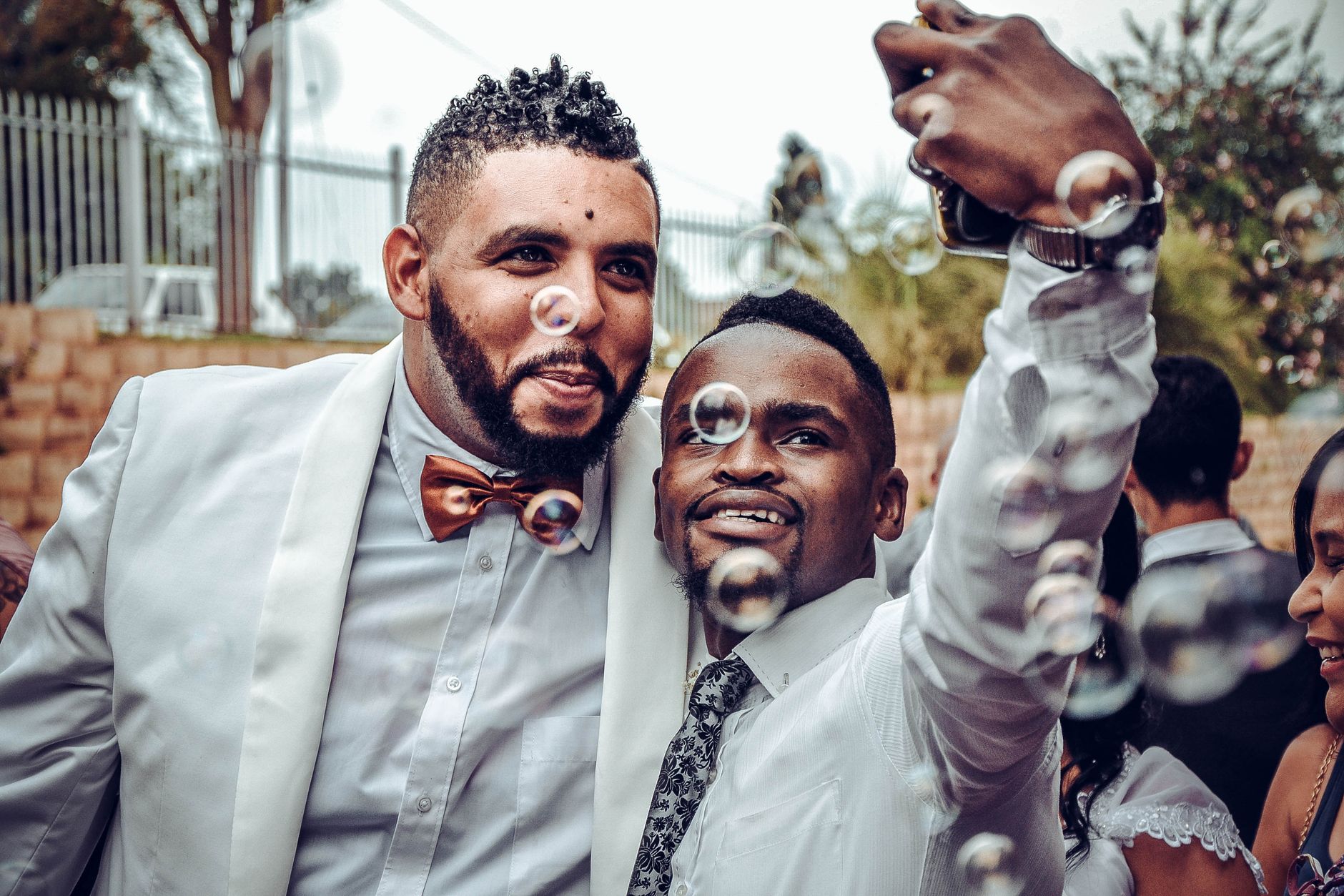 Two men taking a selfie at a wedding, surrounded by bubbles, celebrating joyfully.